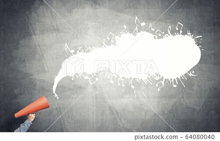 Hand of man holding orange paper trumpet against concrete background Hand of man holding orange paper trumpet against concrete background 64080040