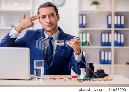 Young male employee and a lot of pills on the desk 64082000