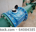 Closeup - of the blue industrial water meter With green metal pipes for supplying water and many fasteners On a cement floor background. Selective focus 64084385