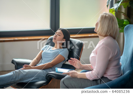 Blonde middle-aged psychiatrist talking to her female patient 64085236