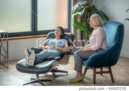 Blonde middle-aged psychiatrist sitting next to a female patient 64085238