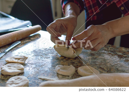 Woman cooking pies, also known as somsa, at home, making food from dough Woman cooking pies, also known as somsa, at home, making food from dough 64086622