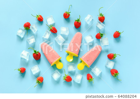 Homemade popsicles. Natural ice cream in bright plastic molds, strawberries and ice cubes on blue background. Top view Flat lay 64088204