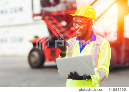Black African happy worker working in logistic communication using radio and laptop Black African happy worker working in logistic communication using radio and laptop 64088260