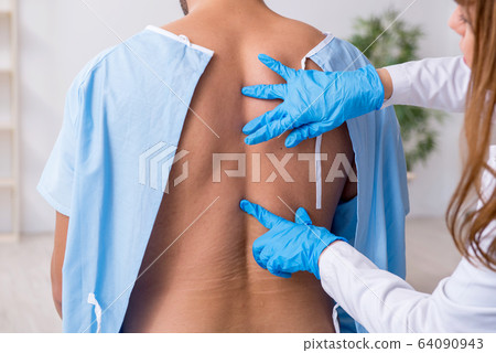 Young back injured man visiting female doctor chiropractor 64090943