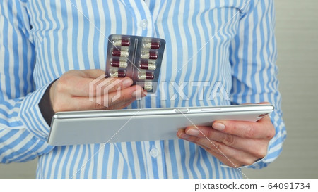 The girl holds a blister with tablets in her hand and uses the tablet to buy medicines through an online store or pharmacy. 64091734