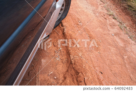 Driving 4wd vehicle on red dusty country road with big holes, detail on tire with low pressure going over rough terrain. Roads are in bad condition on Madagascar, especially after rain 64092483