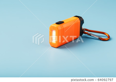 An orange led flashlight with a carabiner glows on An orange led flashlight with a carabiner glows on 64092797