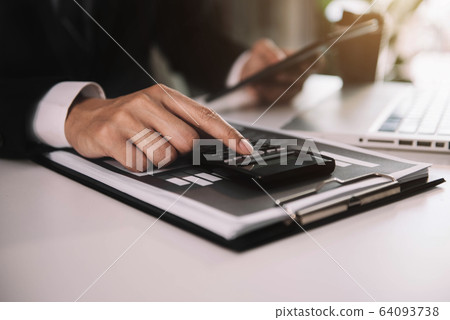 Businessman calculates financials with graph paper on the table on the cost of home office in the evening. Businessman calculates financials with graph paper on the table on the cost of home office in the evening. 64093738