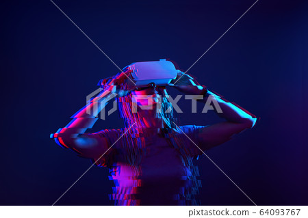 Woman is using virtual reality headset. Neon light studio portrait. Image with glitch effect. 64093767