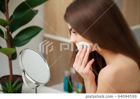 Cute woman in bathroom doing cosmetic procedure for facial skin care 64094599
