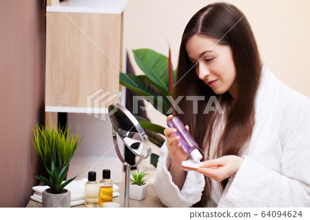 Cute woman in bathroom doing cosmetic procedure for facial skin care Cute woman in bathroom doing cosmetic procedure for facial skin care 64094624