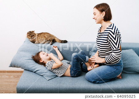 Young attractive woman with her little preschooler daughter having fun at home on couch Young attractive woman with her little preschooler daughter having fun at home on couch 64095025