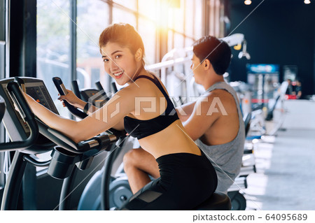 Attractive Asian woman riding on the spinning bike at the gym and looking at camera. Healthy and weight loss lifestyle 64095689