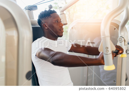 African American athlete doing exercise for chest muscles on pec deck machine during workout in gym African American athlete doing exercise for chest muscles on pec deck machine during workout in gym 64095802