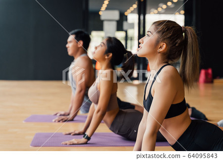 Group of Asian fitness people doing yoga upward facing dog pose on mats at yoga studio. Young women and man exercising at gyn 64095843