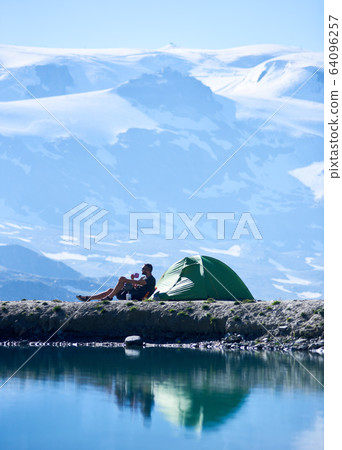 Man drinking tea near tent in mountains. 64096257