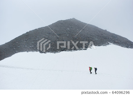 Two hikers walking on snowy path in mountains. 64096296