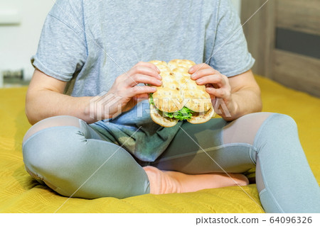 Woman sitting on bed and holding sandwich Woman sitting on bed and holding sandwich 64096326