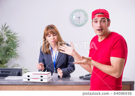 Young male courier delivering pizza to hotel's reception 64096936