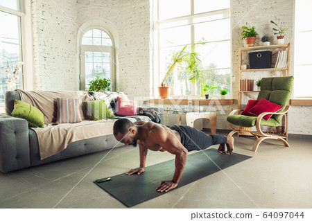 Young african-american man teaching at home online courses of fitness, aerobic, sporty lifestyle while being quarantine Young african-american man teaching at home online courses of fitness, aerobic, sporty lifestyle while being quarantine 64097044