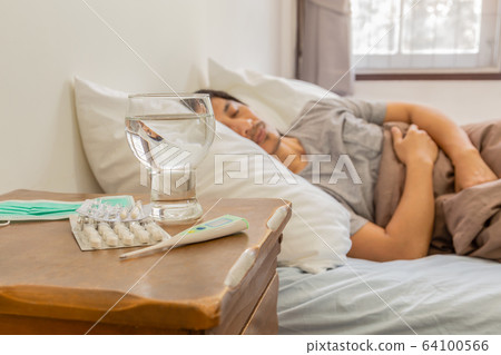 Pills and glass of water, Thermometer on tablets with man sleeping in bed. 64100566
