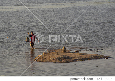 Little boy planting traditional fish trap in a shallow part of Mekong River, Ubon Ratchathani, Thailand Little boy planting traditional fish trap in a shallow part of Mekong River, Ubon Ratchathani, Thailand 64102908