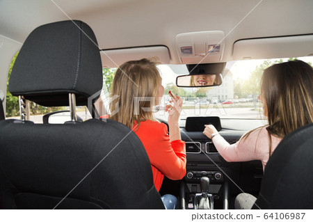 Two young women tune radio and do makeup in car Two young women tune radio and do makeup in car 64106987