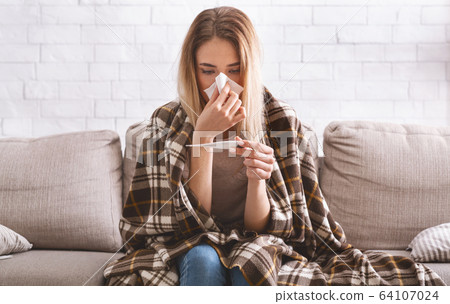 Woman with plaid on shoulders measures temperature 64107024