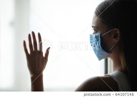 Woman In Medical Mask Standing Near Window Staying At Home Woman In Medical Mask Standing Near Window Staying At Home 64107148