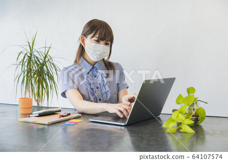 Woman working remotely with mask on Woman working remotely with mask on 64107574