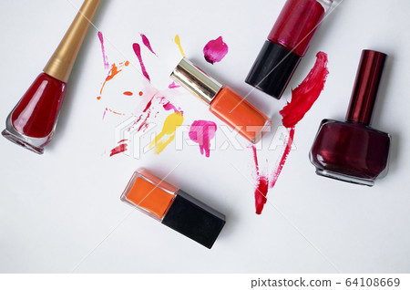 Lucky on a white background, with smears of varnish. Orange, burgundy, red.Choosing varnishes for manicures in a beauty salon. 64108669