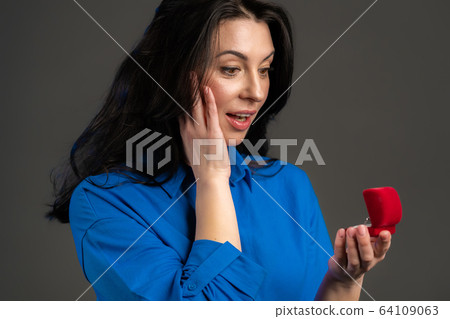 Attractive european adult surprised and shocked woman holding small jewelry box with proposal Attractive european adult surprised and shocked woman holding small jewelry box with proposal 64109063
