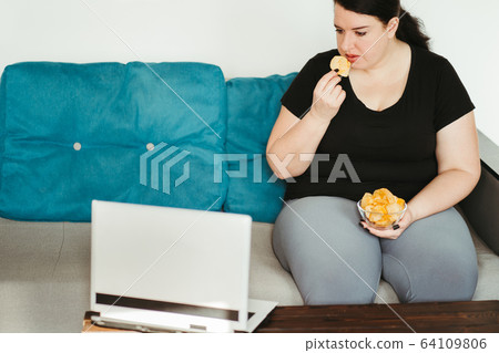 Woman eating unhealthy food watching series online 64109806