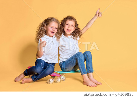 Two Active and happy girls with curly hair having fun with penny board, smiling face stand skateboard. Penny board cute skateboard for girls. Lets ride. Girl with penny board yellow background Two Active and happy girls with curly hair having fun with penny board, smiling face stand skateboard. Penny board cute skateboard for girls. Lets ride. Girl with penny board yellow background 64109853