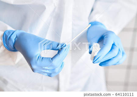 Doctor holding swab test tube for 2019-nCoV analyzing. Coronavirus test. Blue medical gloves and protective face mask for protection against covid-19 virus. Coronavirus and pandemic. 64110111