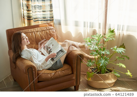 Young woman by window sofa relaxing reading hobby 64121489