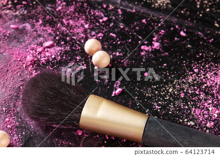 A make-up brush with broken cosmetics and pearls on a black background with a place for text 64123714