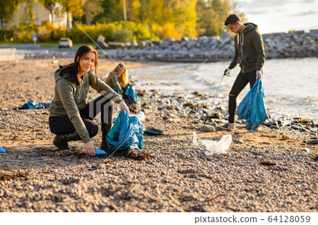 Young woman picking up garbage in bag at beach Young woman picking up garbage in bag at beach 64128059