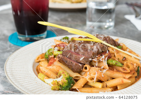 Macaroni with steak and tomato sauce on the table. Macaroni with steak and tomato sauce on the table. 64128075