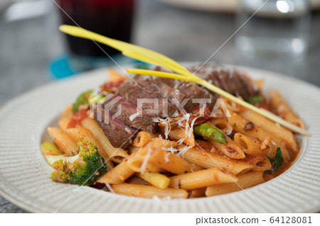 Macaroni with steak and tomato sauce on the table. 64128081