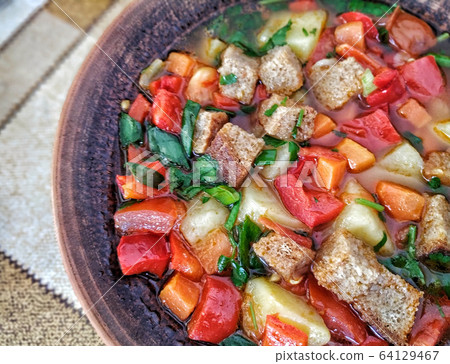 Clay plate with mix colourful vegetable soup or stew and crackers top view Clay plate with mix colourful vegetable soup or stew and crackers top view 64129467