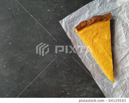 A piece of pumpkin cheesecake on white crumpled paper on a black granite chalkboard with text space A piece of pumpkin cheesecake on white crumpled paper on a black granite chalkboard with text space 64129583