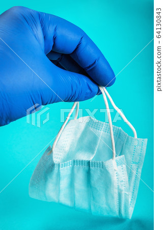 rubber-gloved hand holds a disposable face mask 64130843