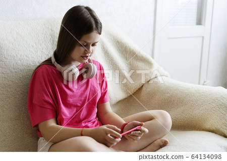 Cheerful girl in pink headphones sits with a phone in her hand Cheerful girl in pink headphones sits with a phone in her hand 64134098