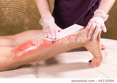 Waxing woman leg. Salon wax beautician epilation procedure. Waxing female body for hair removal by therapist close up. Smooth legs concept. Waxing woman leg. Salon wax beautician epilation procedure. Waxing female body for hair removal by therapist close up. Smooth legs concept. 64135004