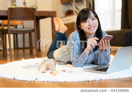 Young woman looking at smartphone while lying in the living room 64136988