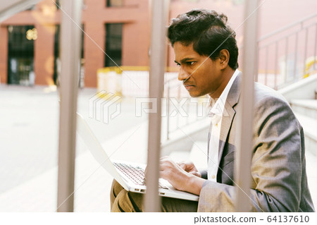 Young handsome Indian man in a white shirt and a business suit is sitting Young handsome Indian man in a white shirt and a business suit is sitting 64137610