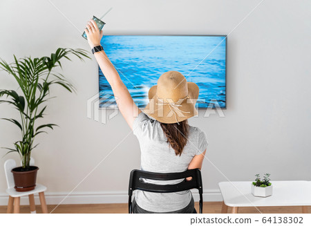 Woman at home pretending to be on the beach. TV screen. 2020 summer quarantine travel. Stay home Woman at home pretending to be on the beach. TV screen. 2020 summer quarantine travel. Stay home 64138302