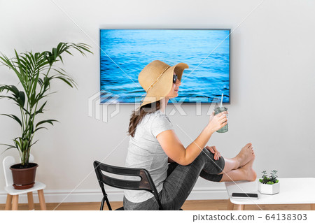 Woman at home pretending to be on the beach. TV screen. 2020 summer quarantine travel. Stay home Woman at home pretending to be on the beach. TV screen. 2020 summer quarantine travel. Stay home 64138303